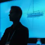 Eine Person in Silhouette steht vor einem hellblauen Hintergrund mit dem Bild eines Segelboots, das auf ruhigem Wasser treibt.