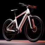 Ein schlankes, modernes, weißes Elektrofahrrad mit minimalistischem Design steht vor einem dunklen Hintergrund, der durch eine dezente rote und weiße Beleuchtung beleuchtet wird, die seine Konturen und Merkmale hervorhebt.