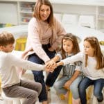 Eine Frau und Kinder sitzen auf Stühlen und legen die Hände übereinander.